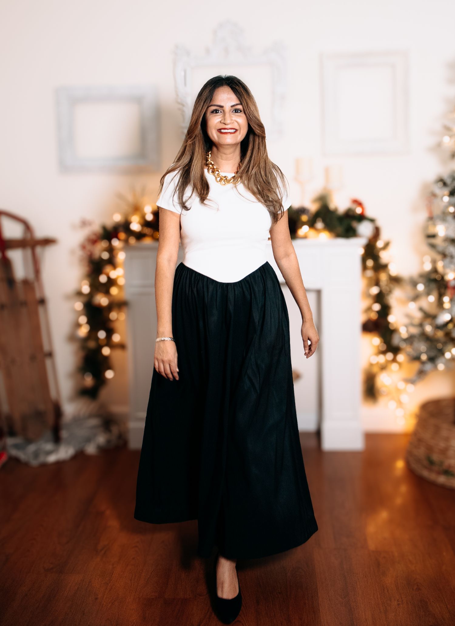 Woman in black dress and white turtleneck twirling in front of Christmas decorations and lights.