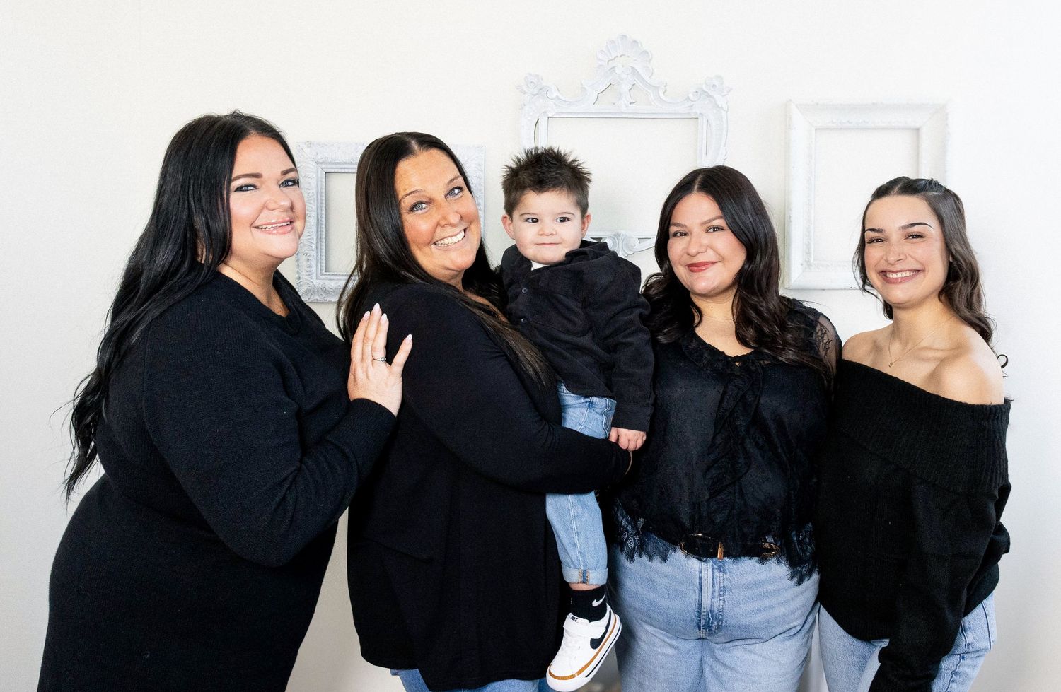 A group wearing black tops and blue jeans poses together in a bright room with a Christmas tree.