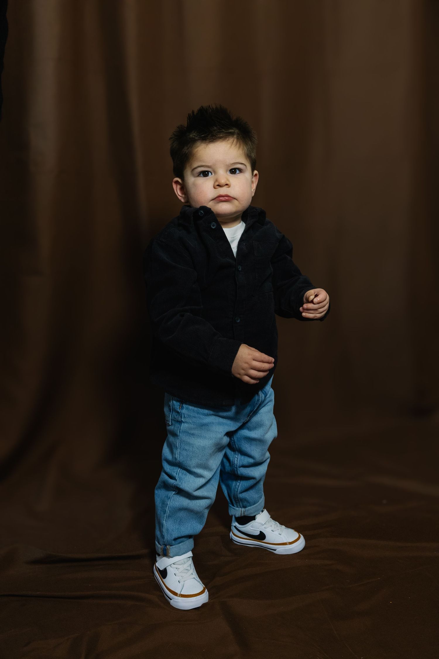 Small child in dark top and jeans stands against brown backdrop in various poses.