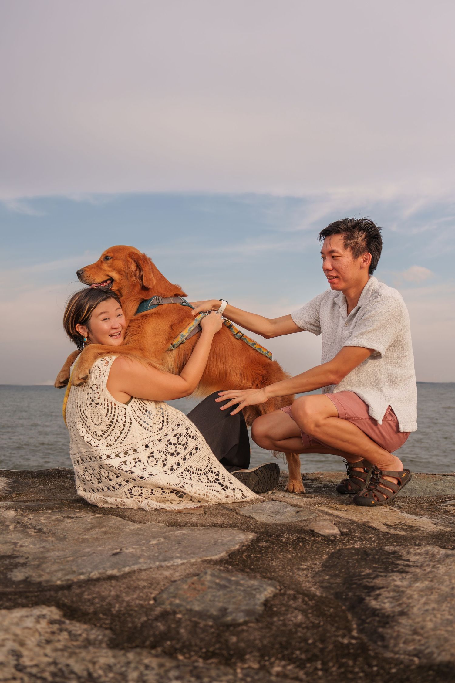 Couple relaxing on beach rocks with their golden retriever dog during sunset by the ocean at East Coast Park Singapore