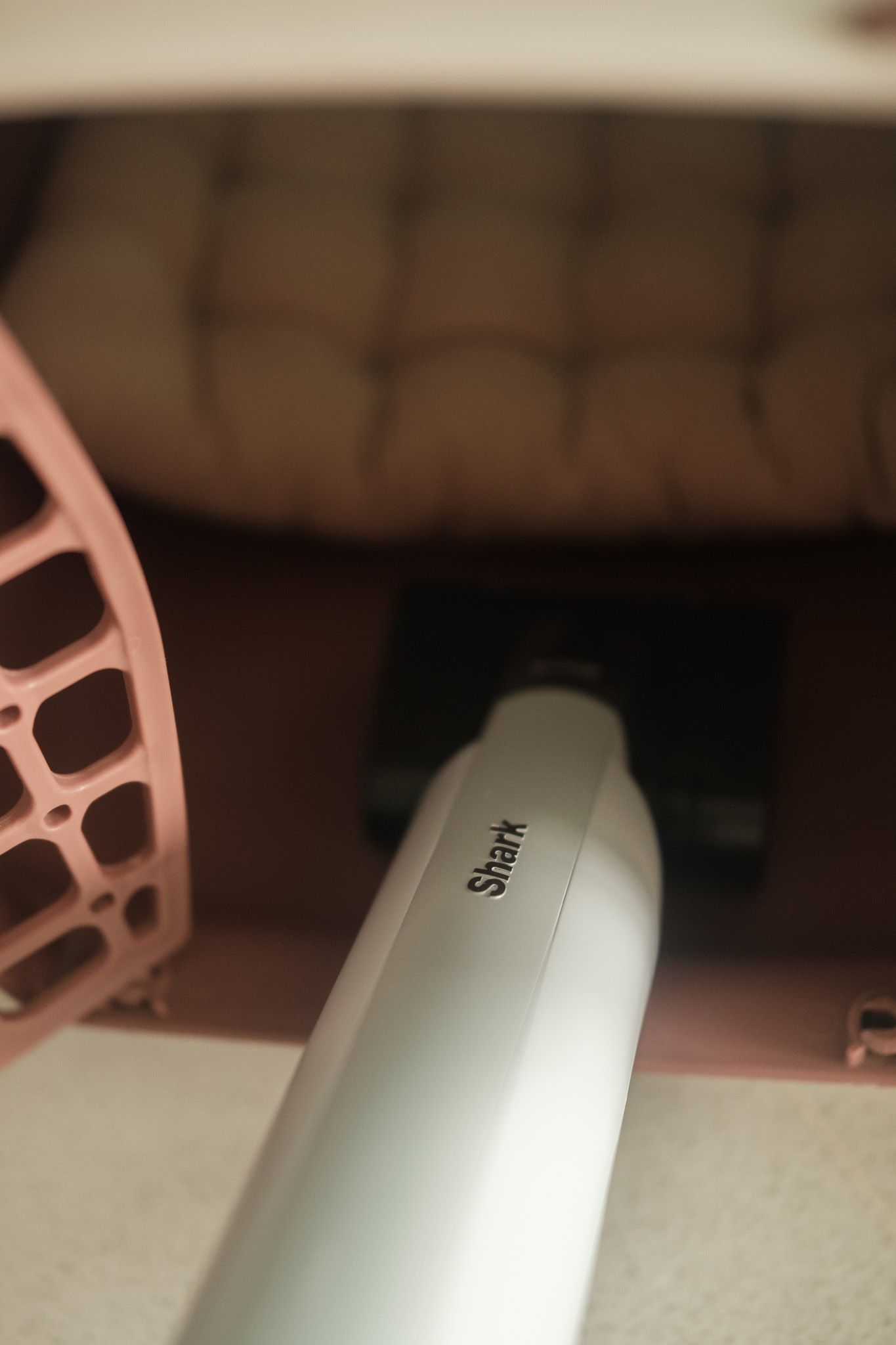 A close-up view of a white Shark brand appliance with a pink accessory visible in the background.
