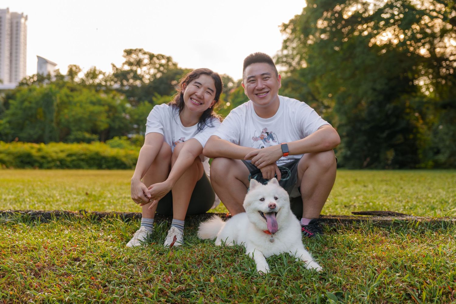 A couple sitting on grass with their white dog during golden hour.