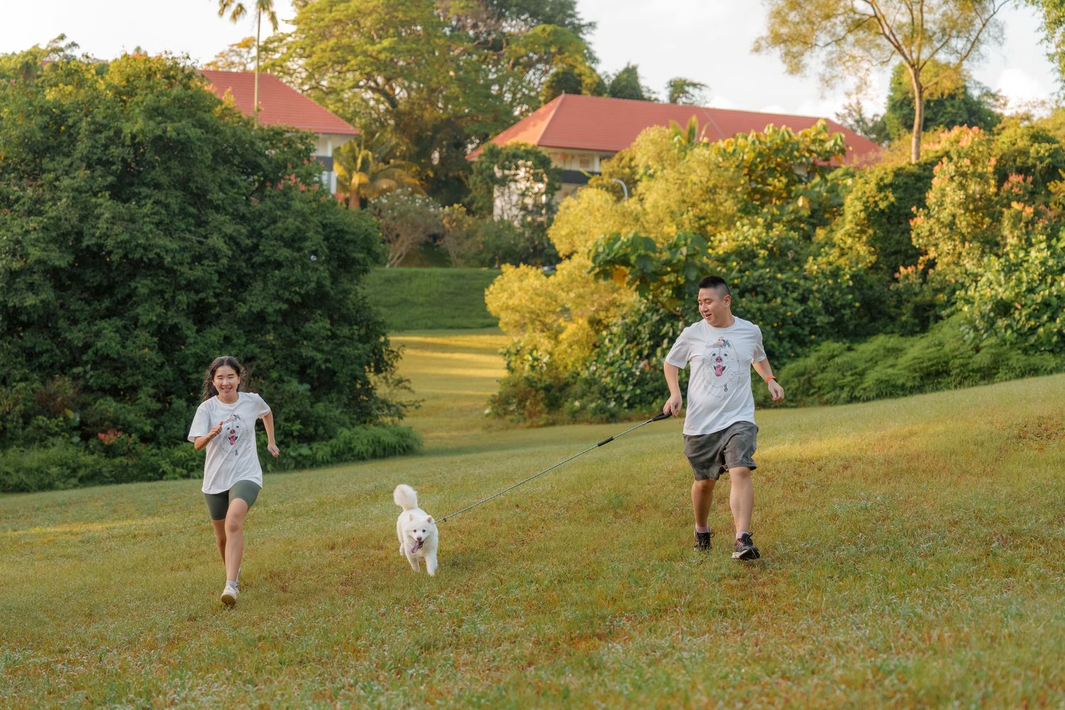 A family running with their white dog on a grassy hill during sunset.