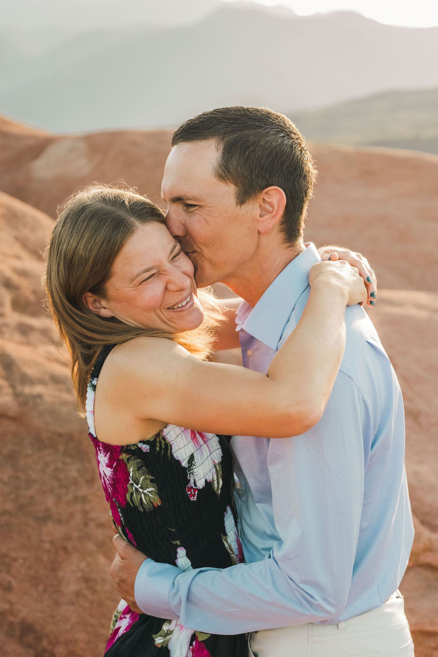 Couple embracing and kissing at red rock canyon during golden hour engagement photo session.