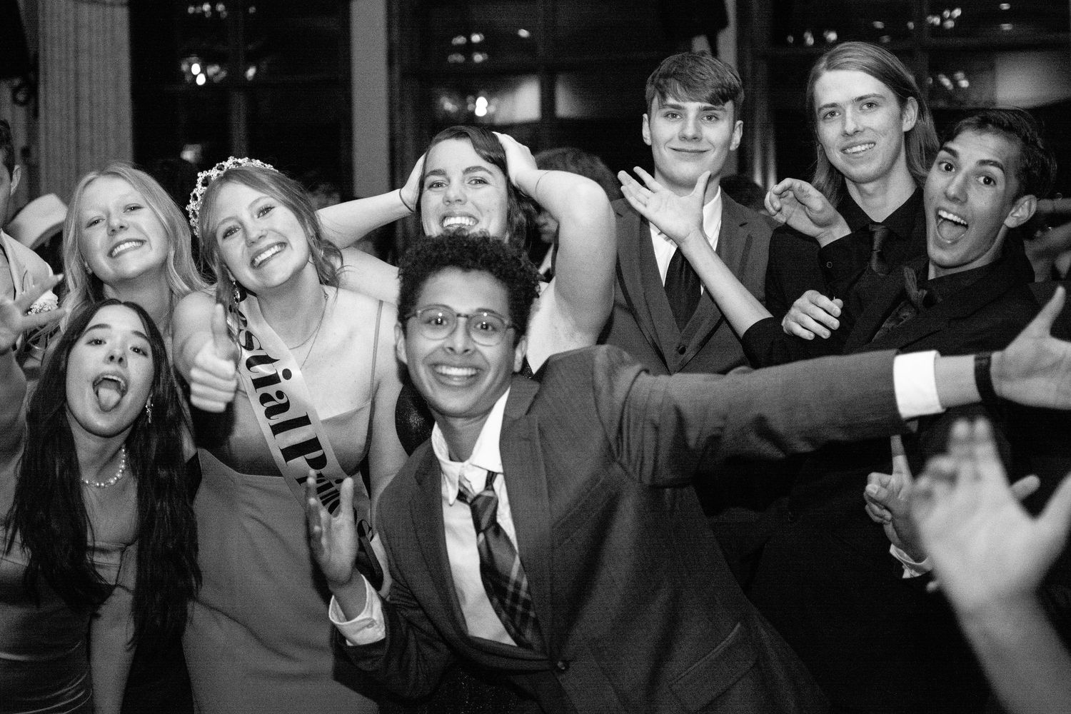 A large group of teenagers celebrate joyfully on a dance floor in black and white photo.