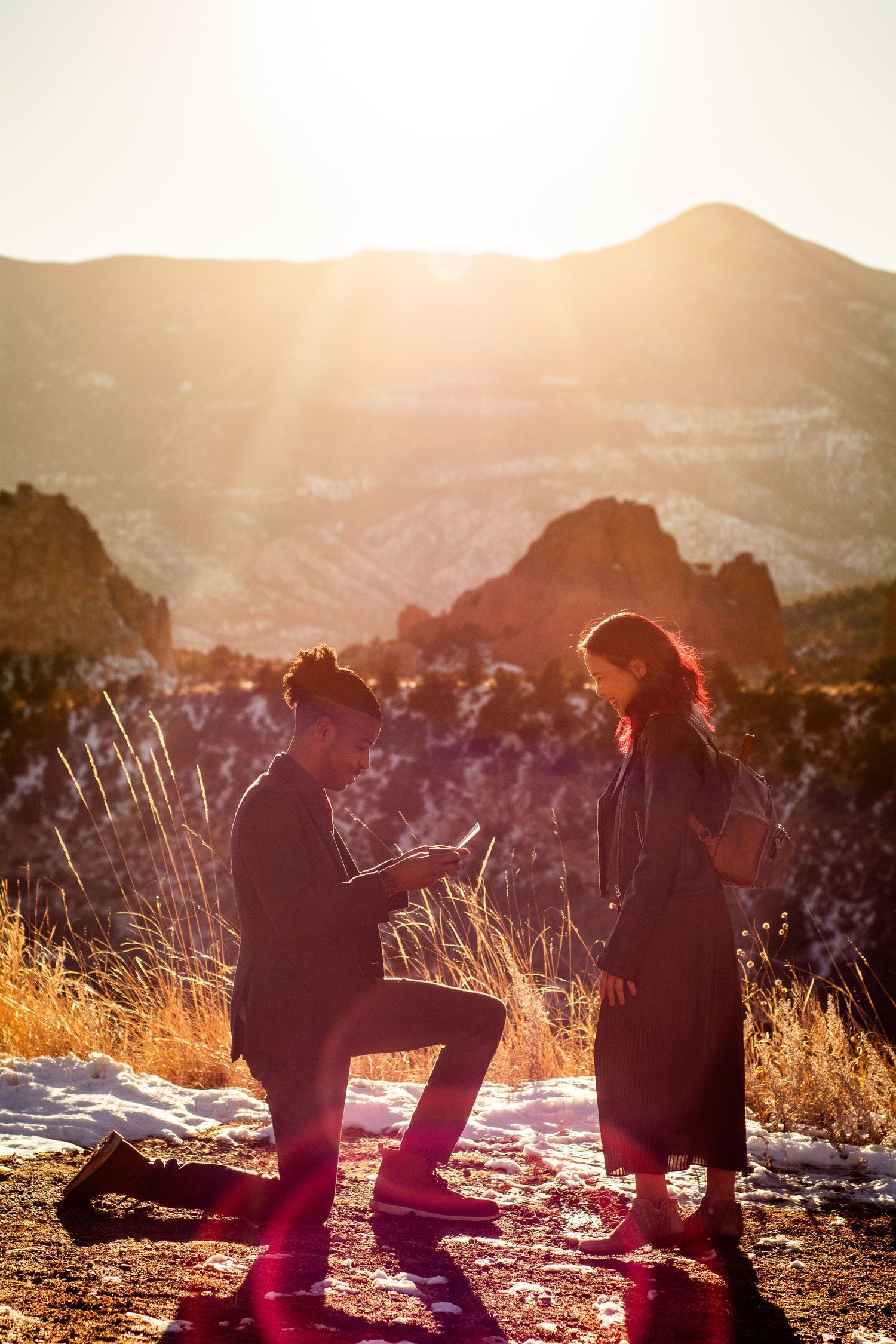 Silhouetted marriage proposal at sunset with red rocks and mountains at Garden of the Gods.
