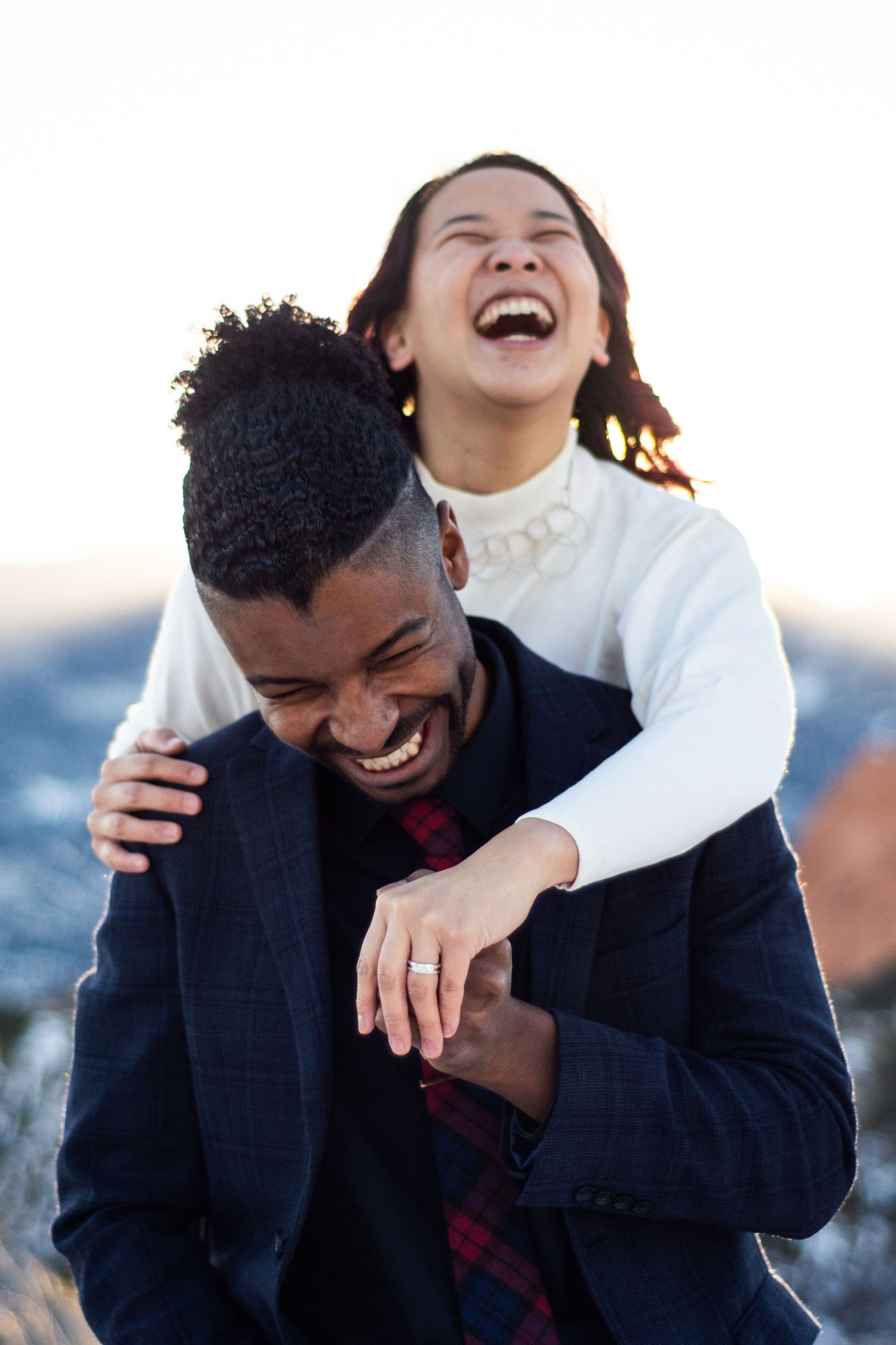 A laughing interracial couple shares a joyful embrace outdoors against a bright winter sky.