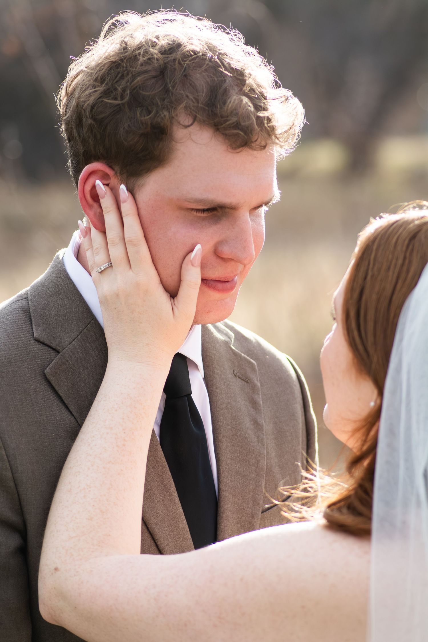Emotional groom being tenderly touched on cheek by bride during outdoor wedding ceremony.