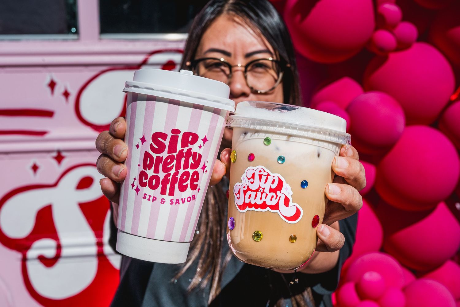 Woman holding two branded Sip Pretty Coffee cups in front of a pink floral backdrop.