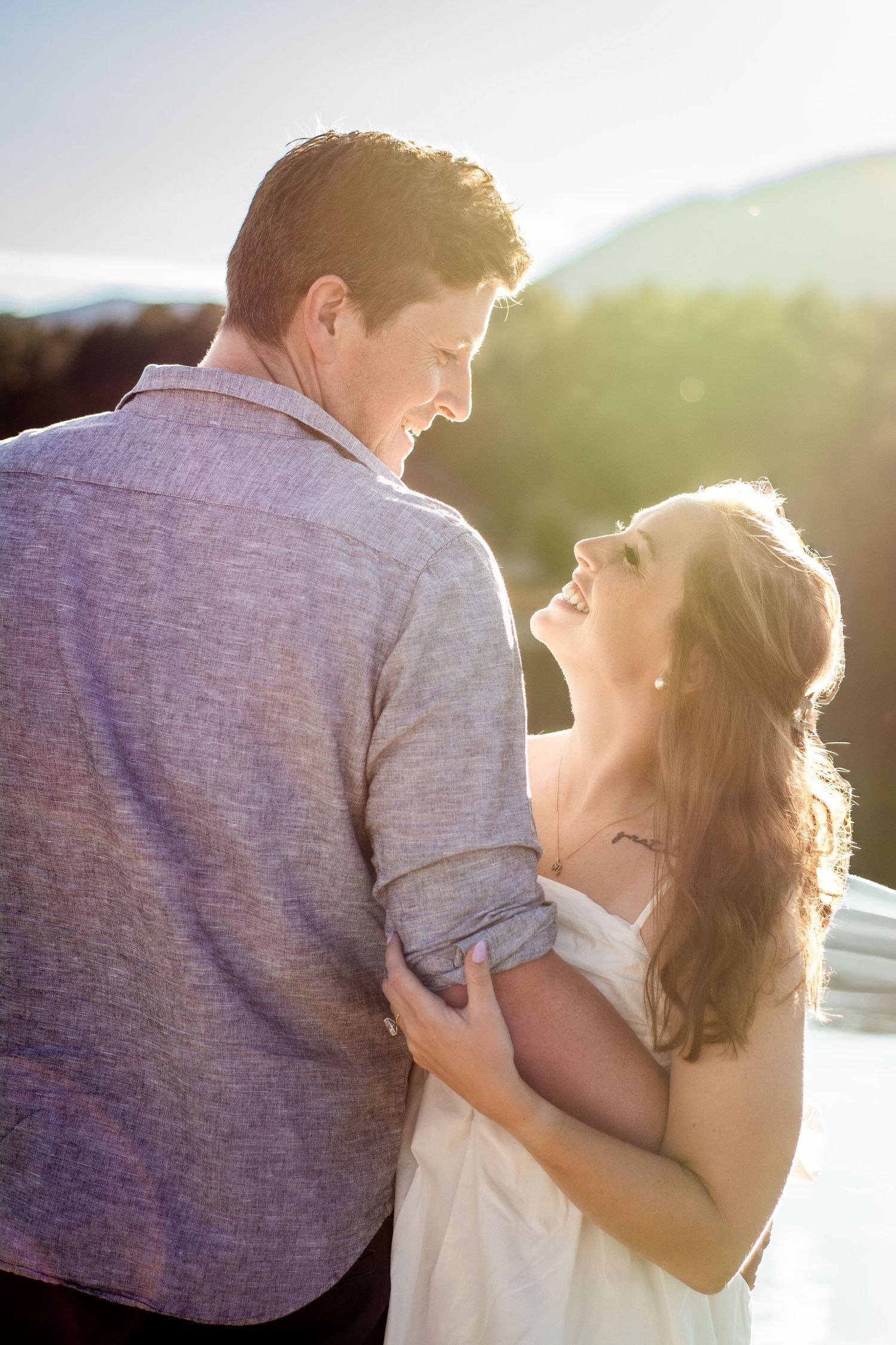 Smiling couple embracing outdoors at golden hour with mountain landscape in background.