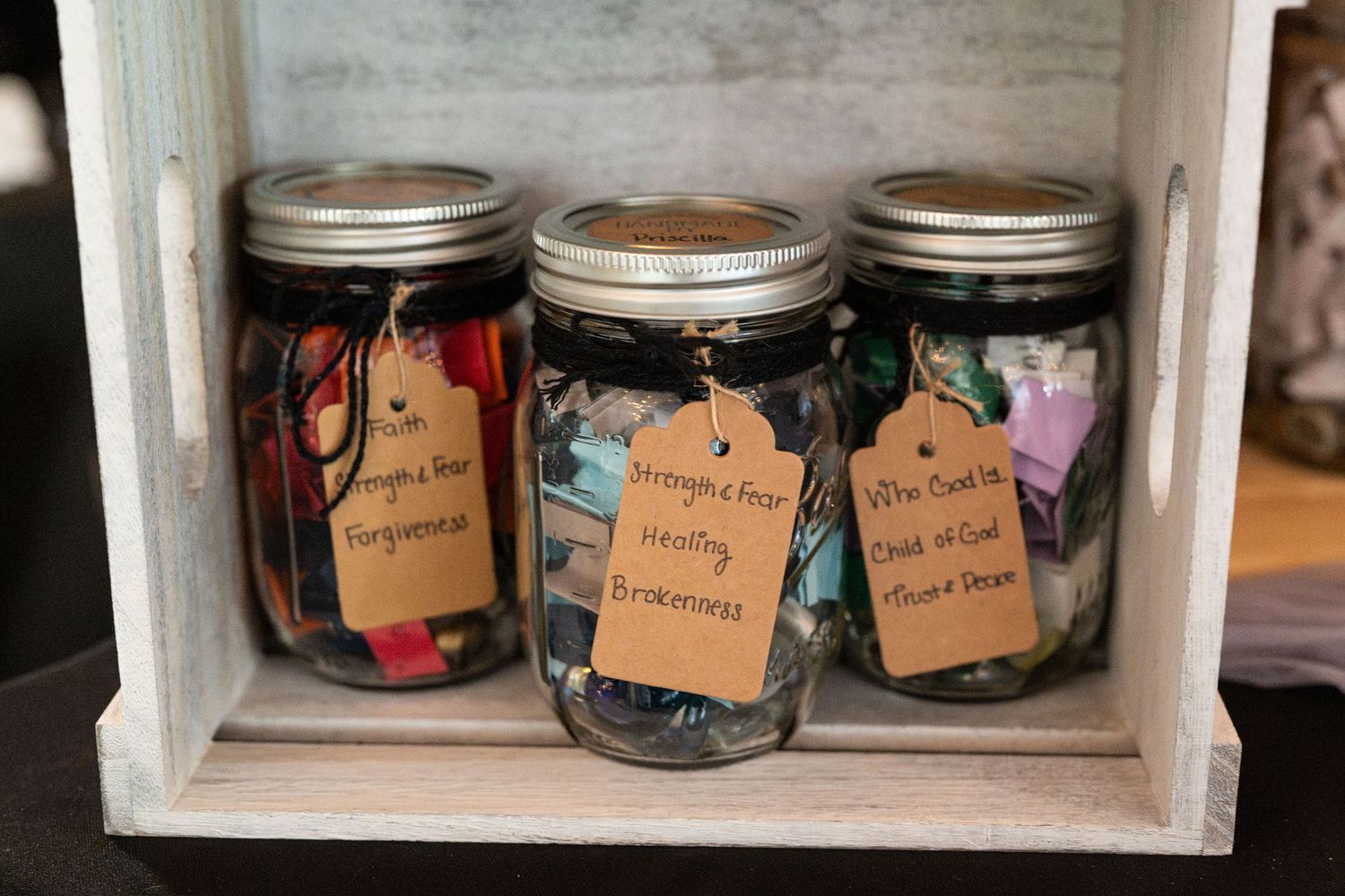 Three Mason jars filled with colorful notes labeled Forgiveness, Brokenness, and Think of God displayed in a wooden crate.