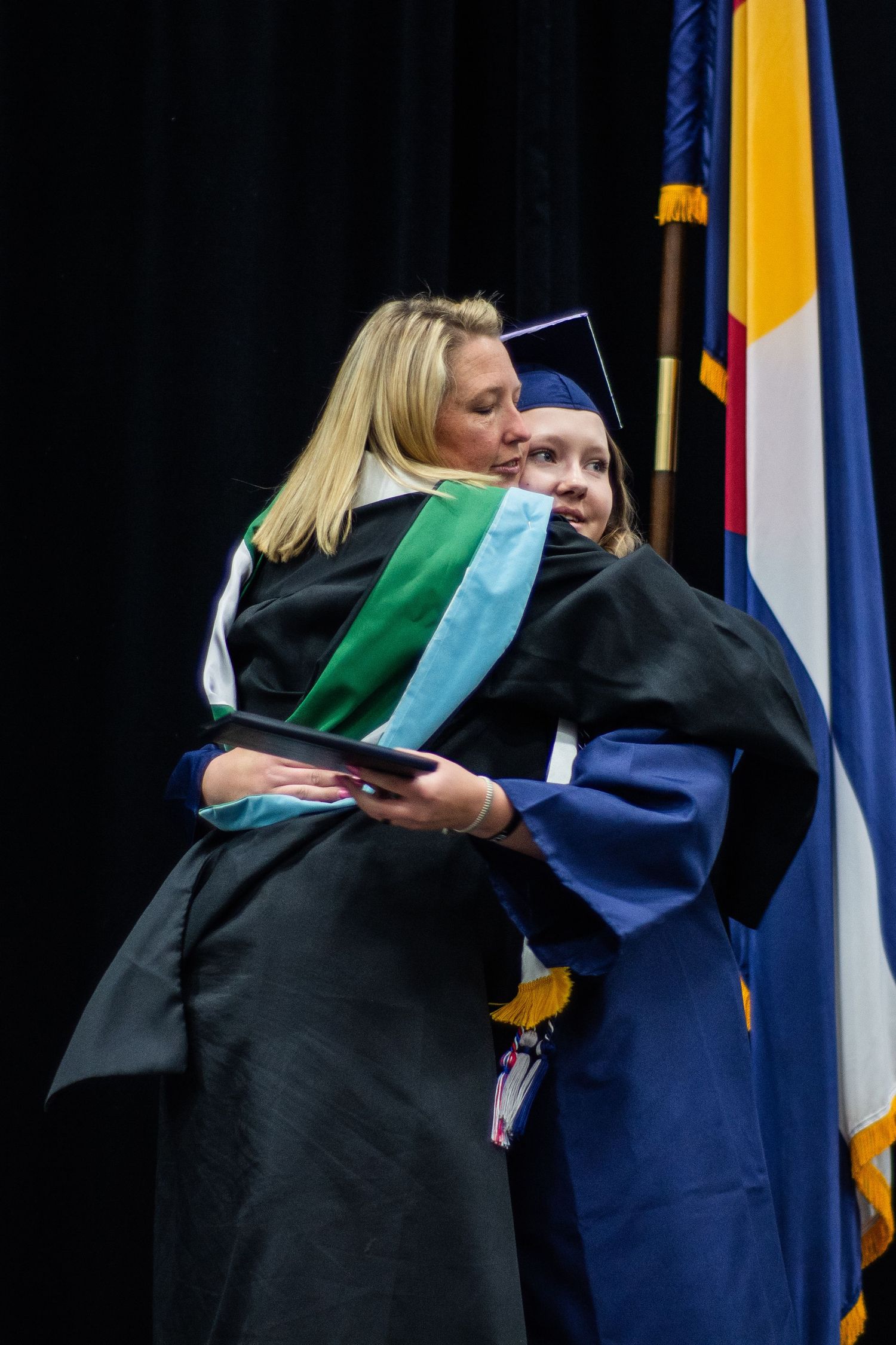 Graduate in navy cap and gown shares warm hug with administrator at commencement ceremony.