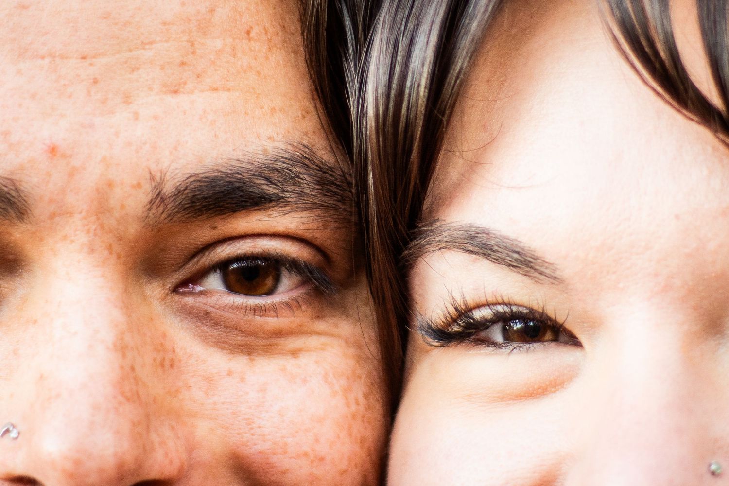 Close-up portrait of two people's eyes side by side, showing diverse skin tones and detailed facial features.