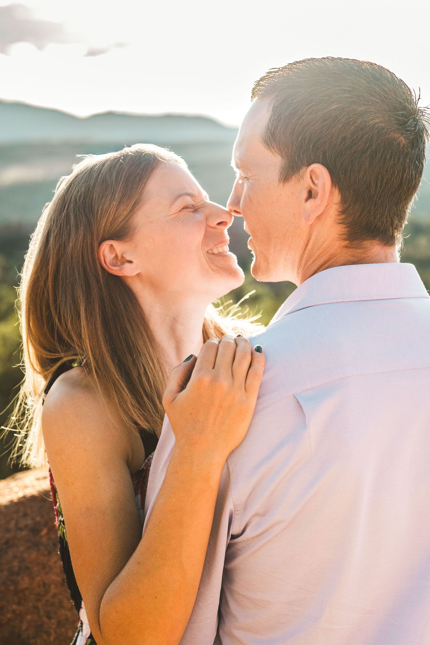 A couple shares a romantic moment outdoors at golden hour, with the woman smiling and touching the mans shoulder.