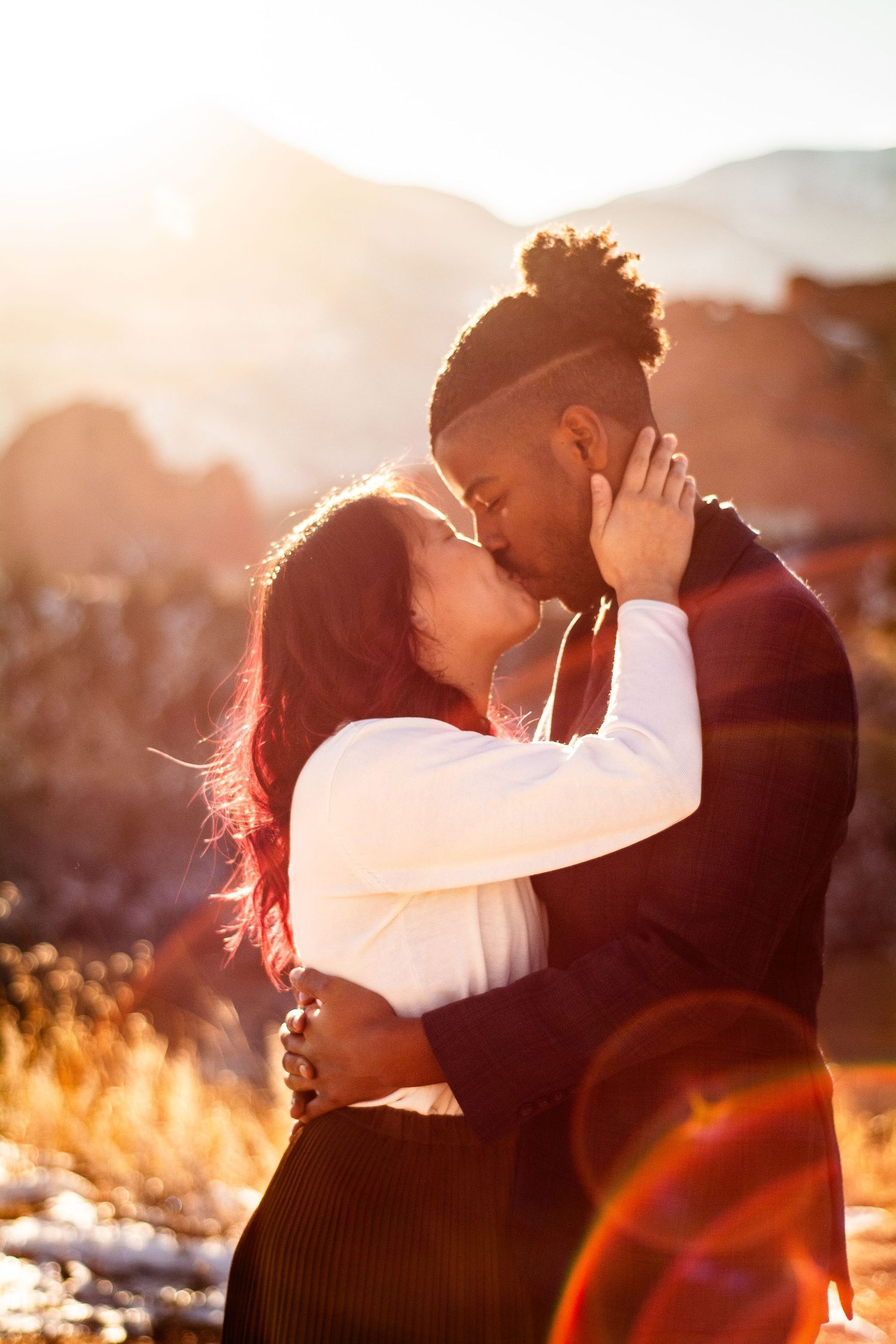 Couple sharing a passionate kiss at golden hour with sunlit mountains in the background.