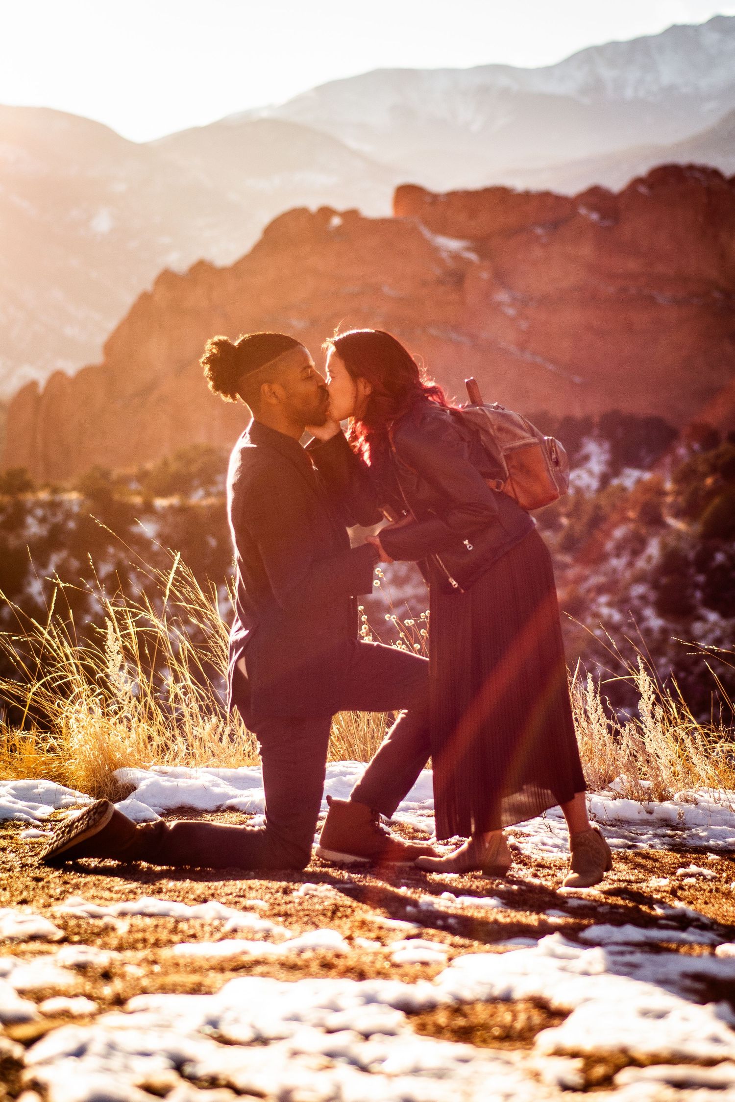 Couple sharing a romantic kiss at Garden of the Gods in winter, with snow-dusted ground and red rock formations at sunset.