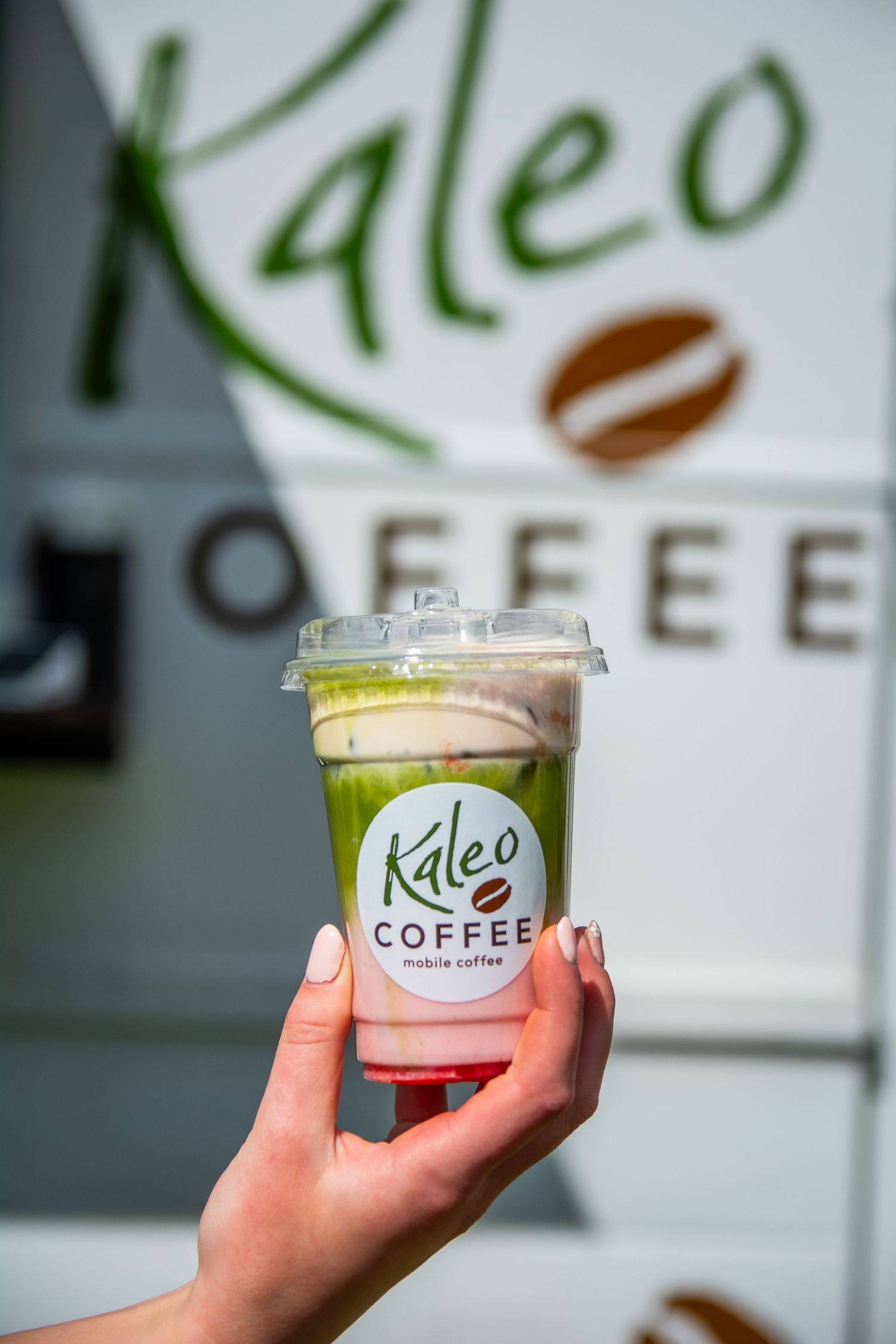 Hand holding Kaleo Coffee mobile coffee cup with green matcha drink in front of branded coffee truck.