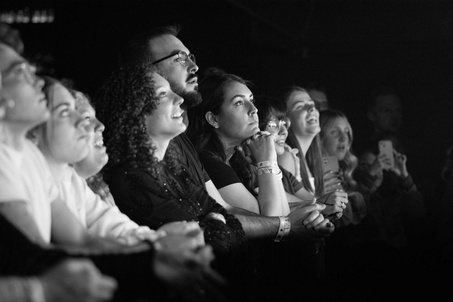Audience members watch attentively at a live event in a black and white photograph.