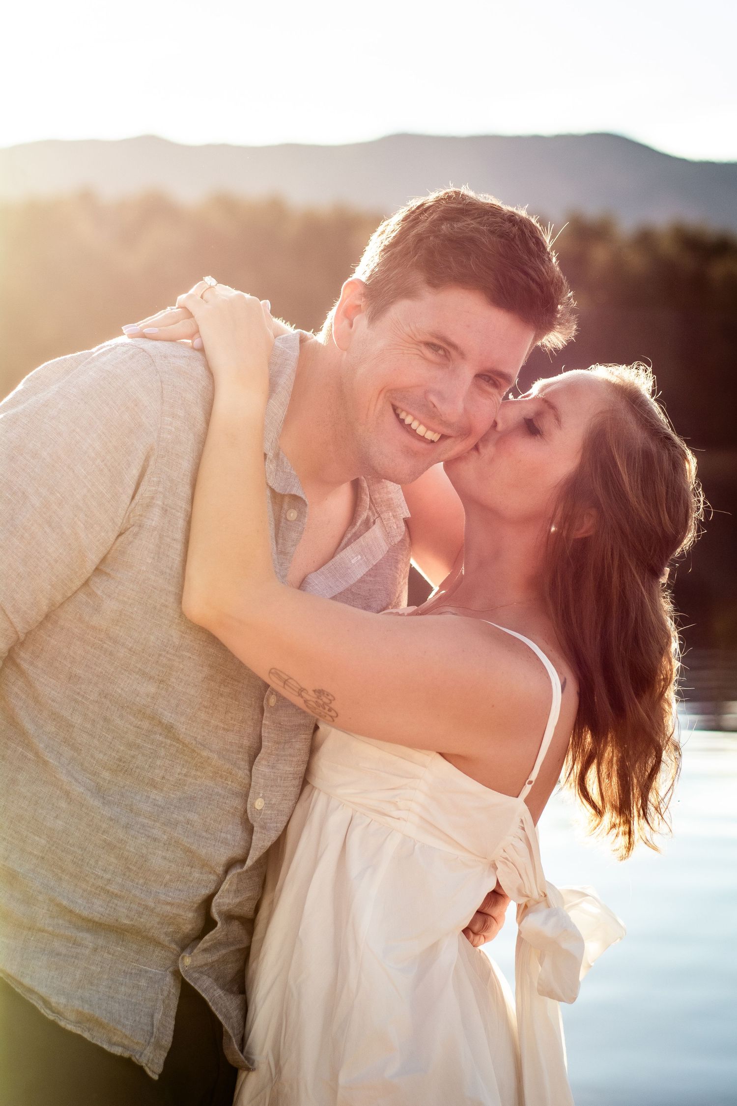 A happy couple sharing a romantic kiss by a lake at golden hour sunset.