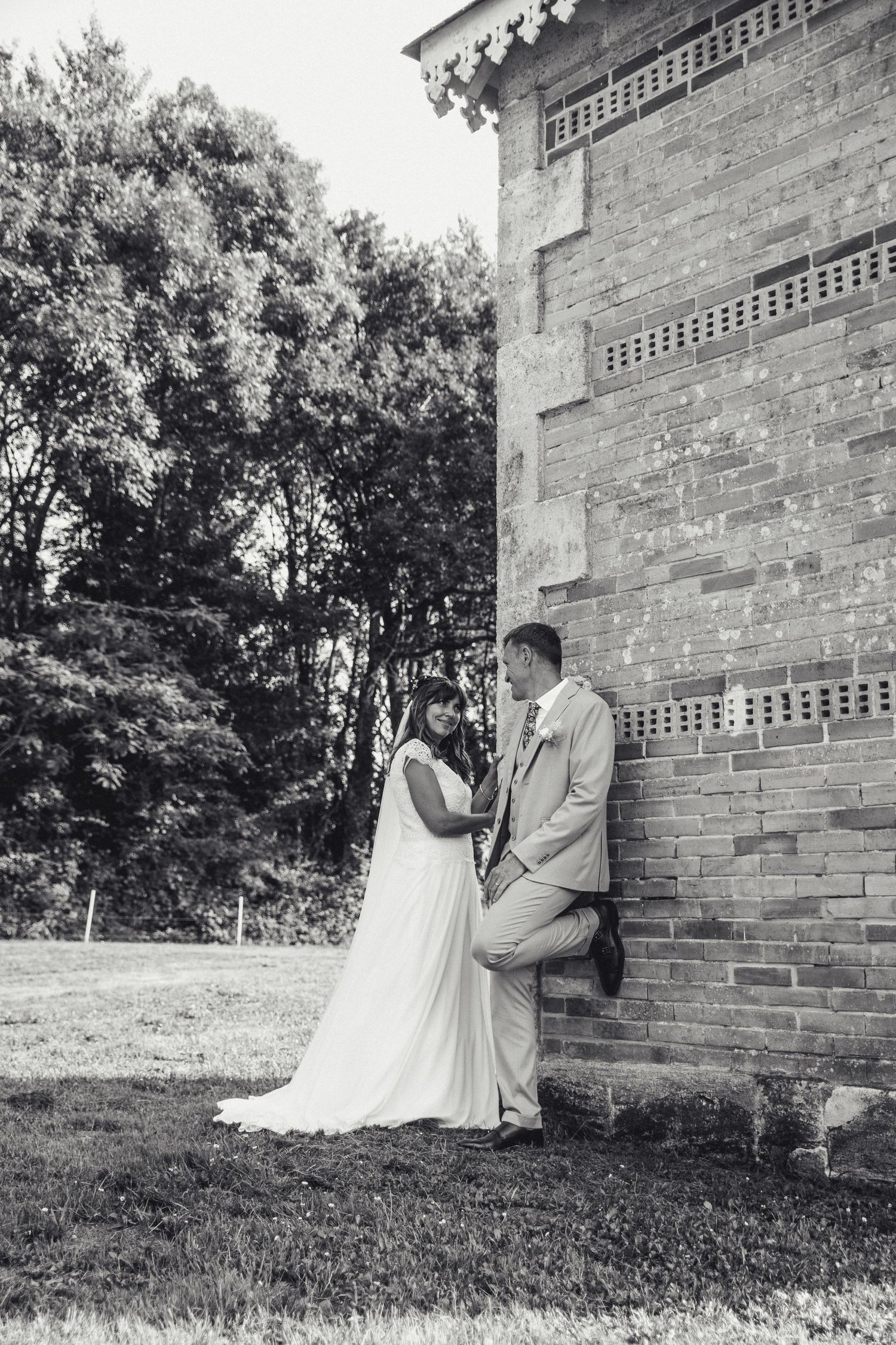 Black and white photos of a couple in wedding attire posing against a brick building exterior.