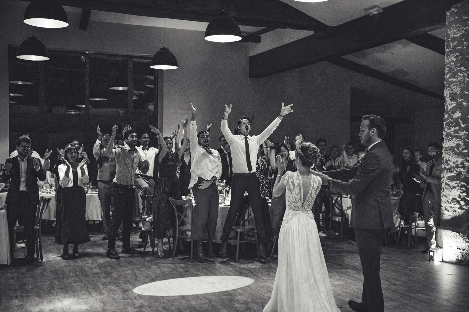 Wedding guests dance and celebrate on a dimly lit dance floor at a reception venue.