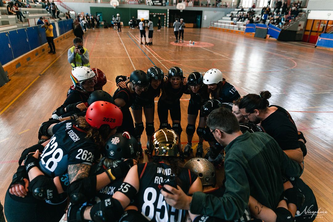 Sports team members huddle together in a gymnasium wearing numbered jerseys.
