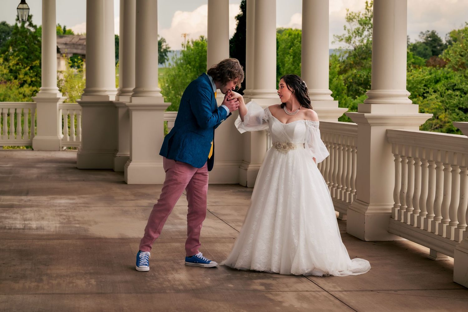 Groom reaching out and kissing bride’s hand as she blushes, about to dance on patio at Huntsville Botanical Garden
