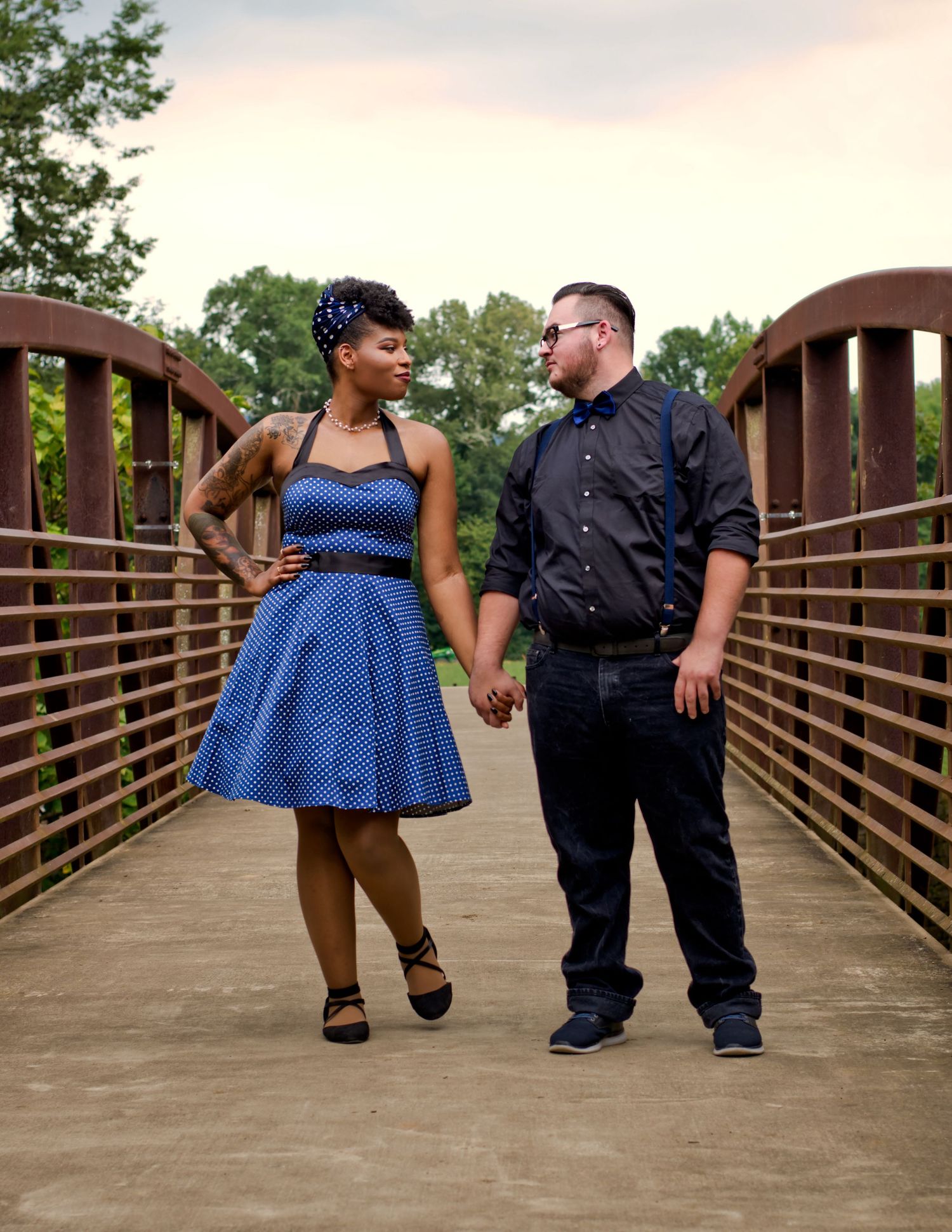 golden hour engagement photo on iron and concrete walking bridge of interracial couple holding hands and looking at each other