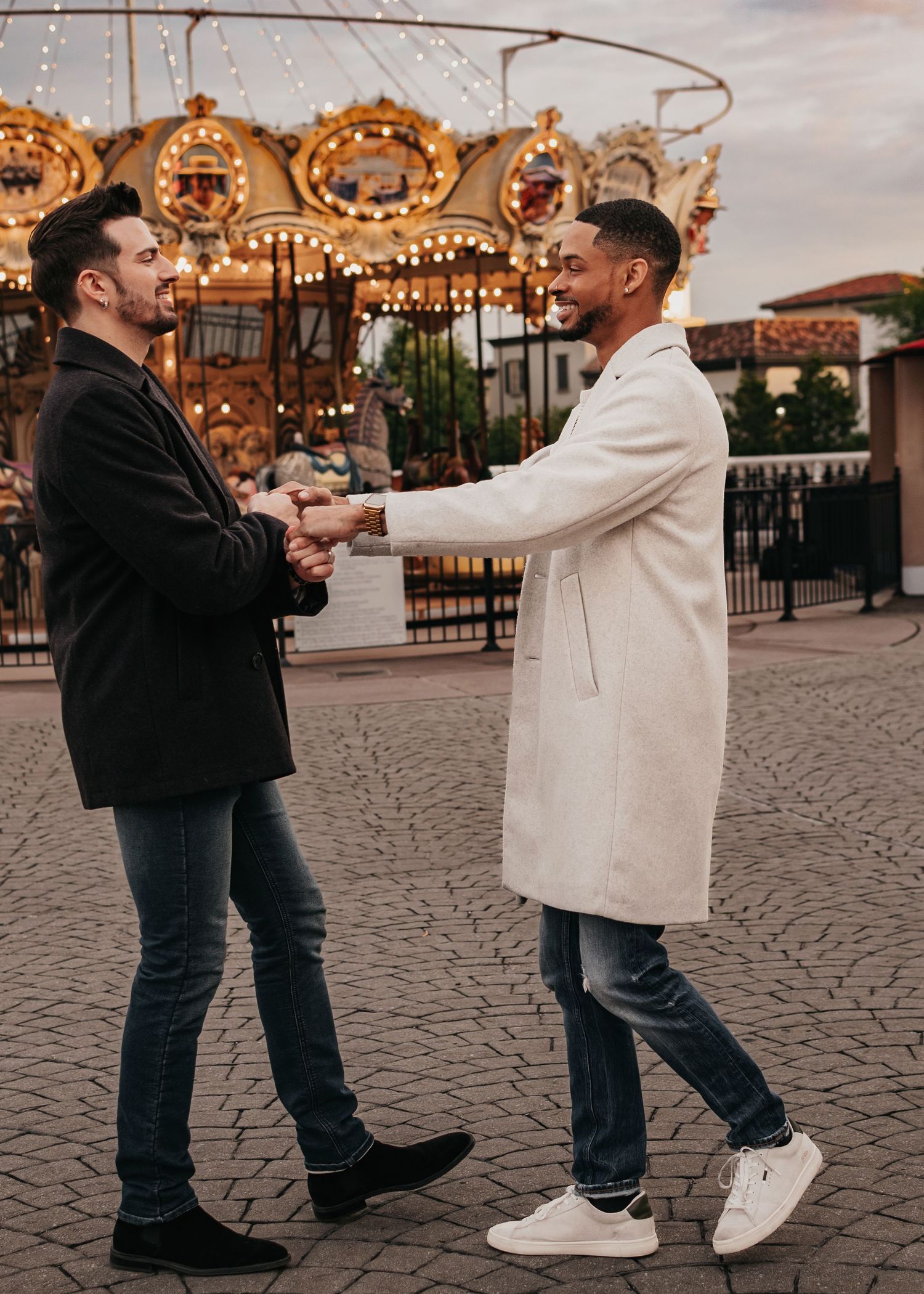 LGBTQ+ couple celebrating engagement beside carousel lights at Bridge Street