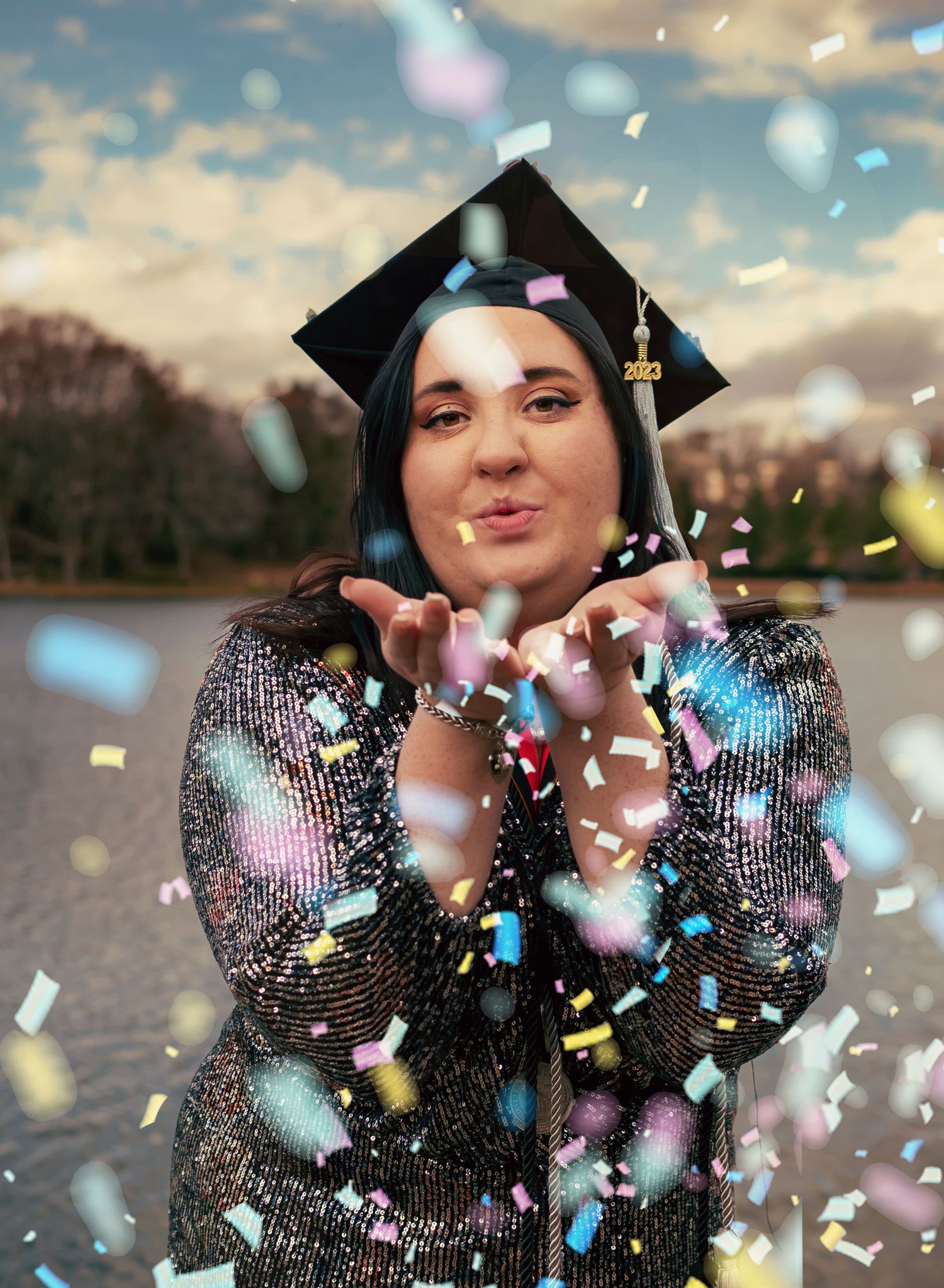 College grad blowing confetti at the camera next to Lady Ann Lake in Huntsville, editorial photo captured by Catch Your Fire Photography.