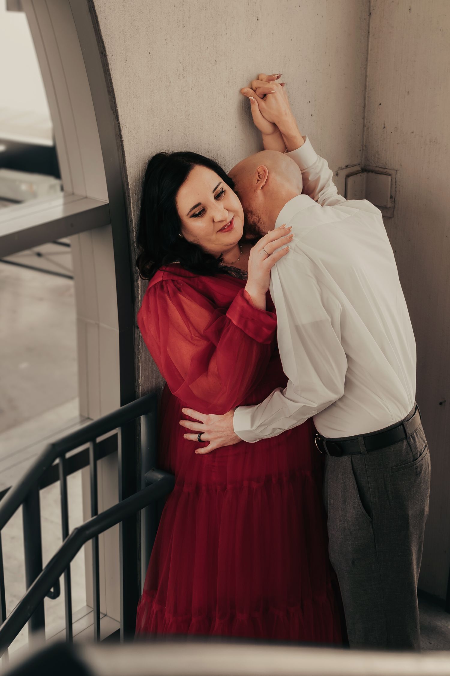 Intimate engagement moment in Bridge Street parking garage stairwell, bride in red gown, captured in cinematic editorial style.