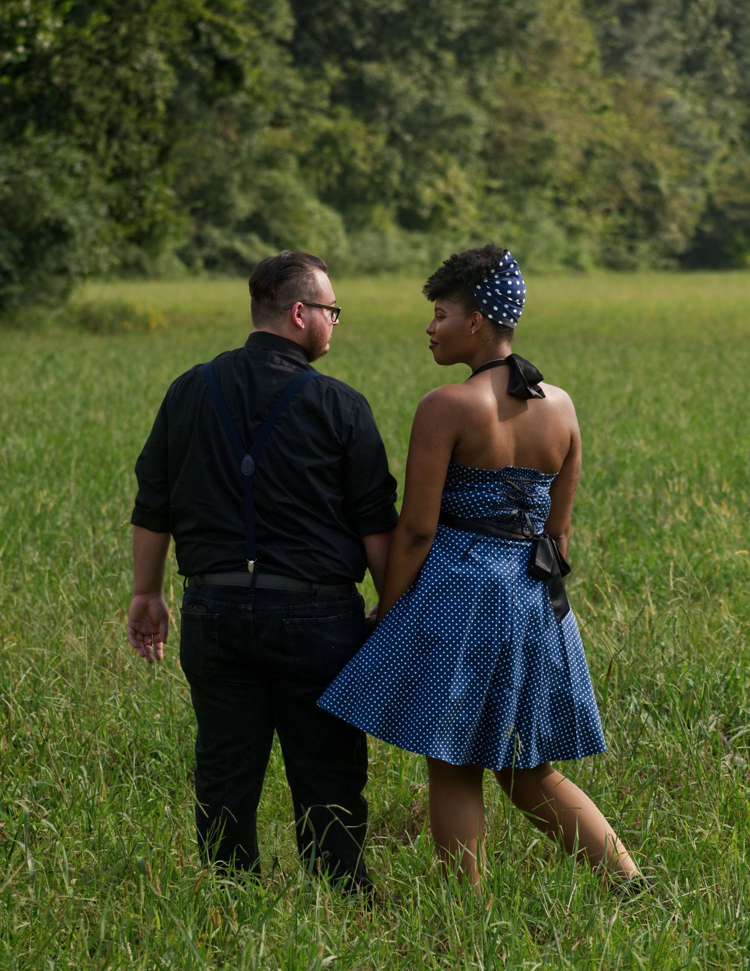 Couple walking hand in hand through lush green field at Hayes Nature Preserve, smiling at each other, by Catch Your Fire Photography.