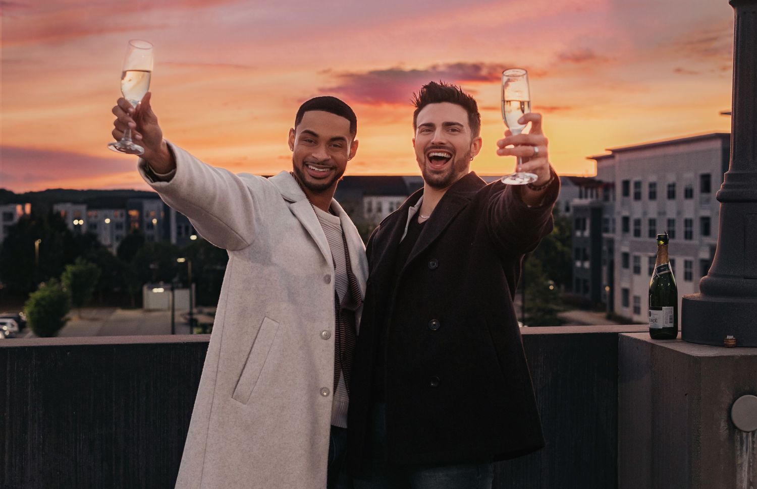 Joyful champagne toast between two grooms at end of rooftop engagement session in Huntsville, Alabama
