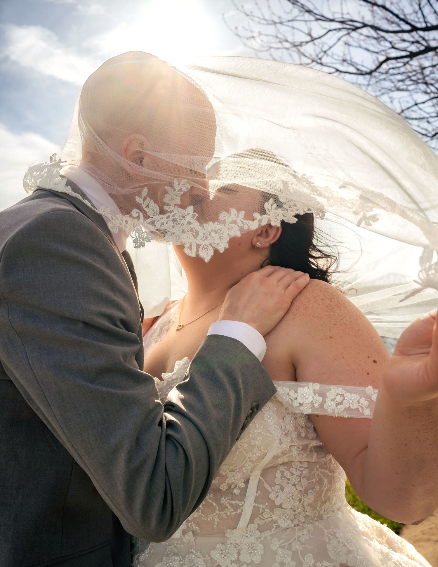 Upward angle of bride and groom kissing behind veil blowing in wind at bright spring wedding, by Huntsville, AL editorial photographers.
