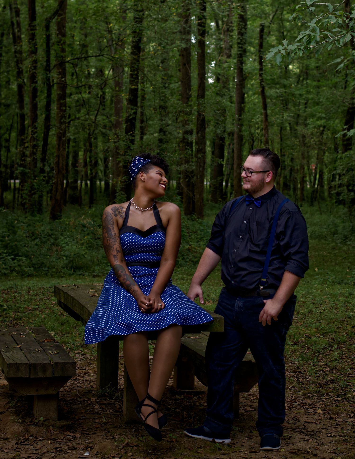 Engagement couple at Hayes Nature Preserve, woman sitting on picnic table, man standing beside her, both smiling at each other.