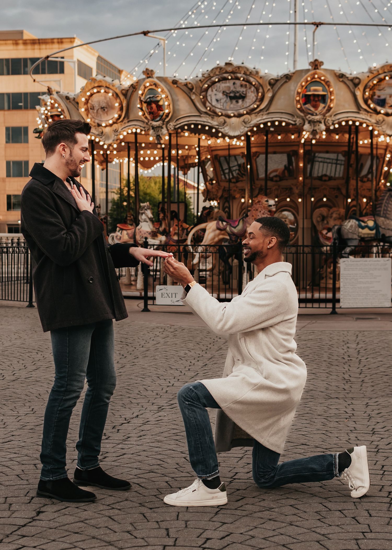 Partner kneeling for LGBTQ proposal in front of carousel, captured by Catch Your Fire Photography at Bridge Street
