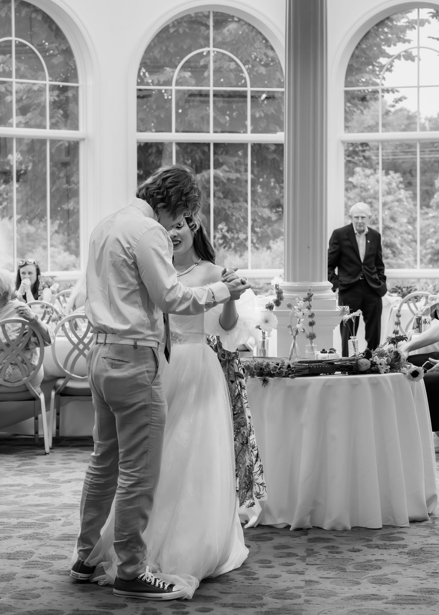 Black and white first dance photo with grandfather lovingly watching the couple during wedding reception
