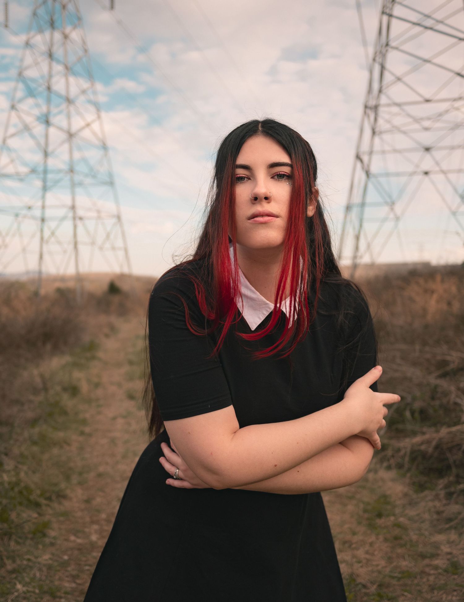 Moody outdoor portrait of girl staring into camera in field with power lines and cloudy blue sky, captured by Catch Your Fire Photography.