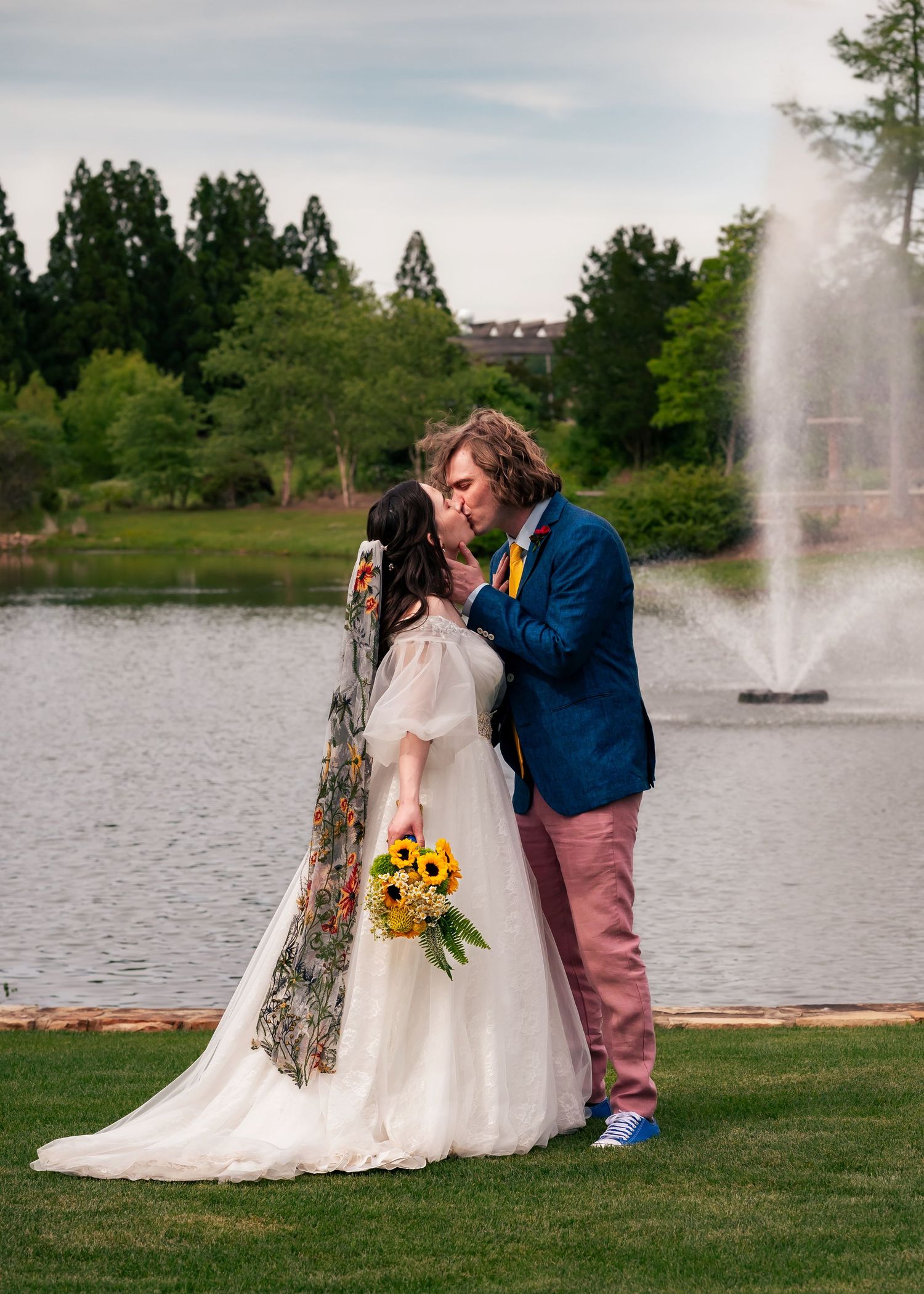 Cinematic, editorial shot of bride and groom kissing in front of pond fountain during romantic spring wedding at Huntsville Botanical Garden