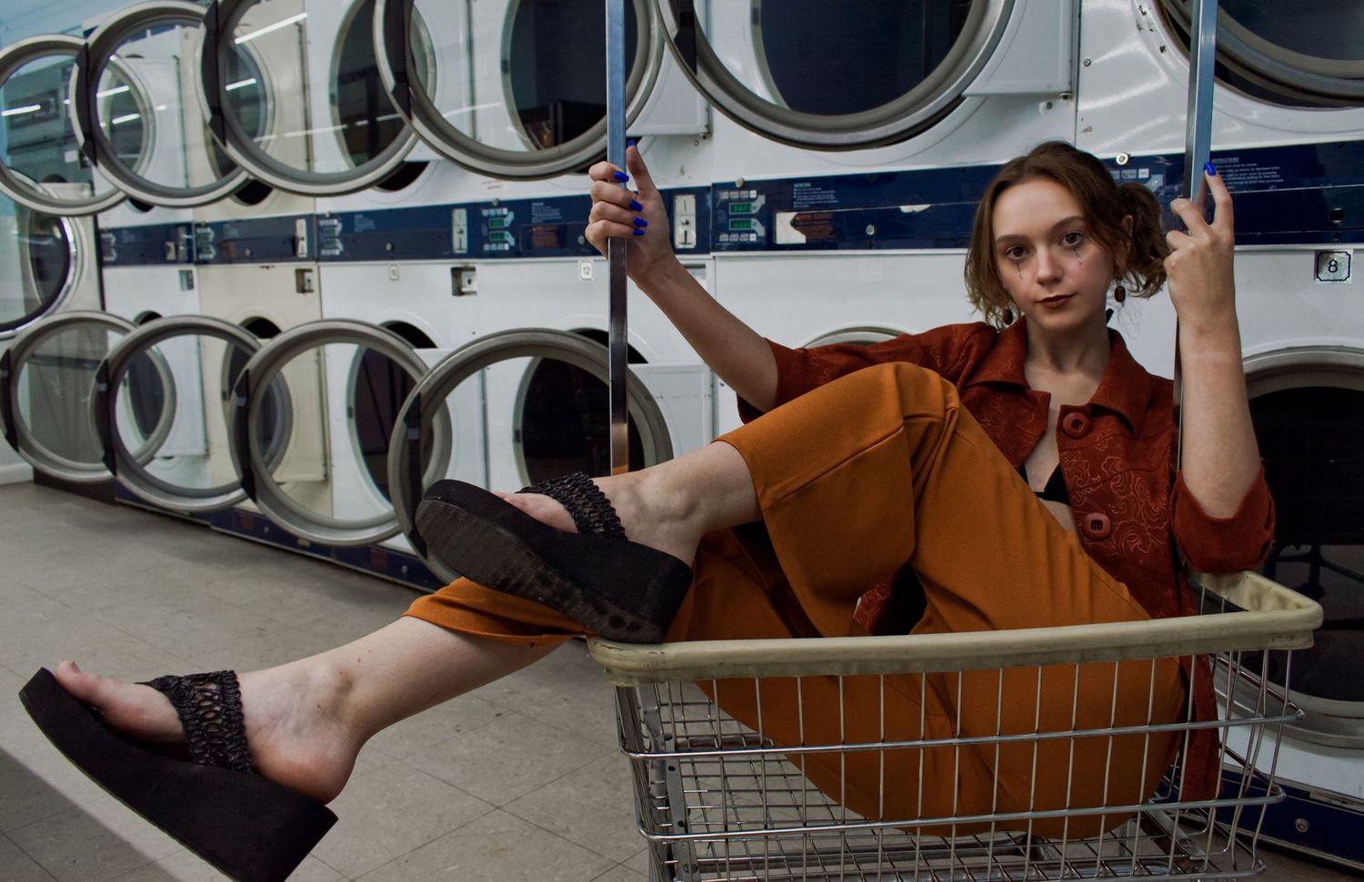 editorial image of a girl riding in a laundry basket in front of rows of open dryers at laundromat in Athens, AL by Catch Your Fire Photo