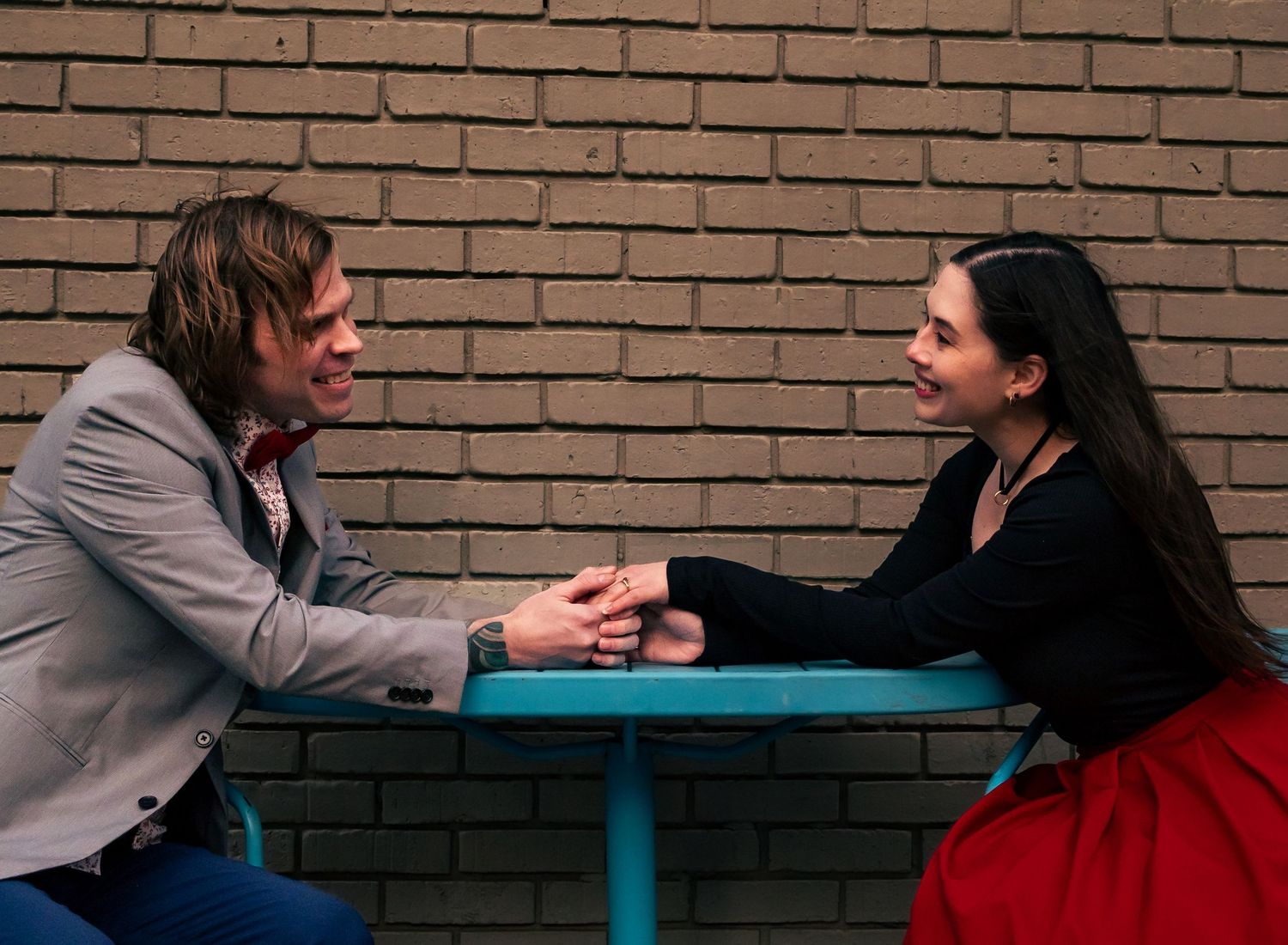 couple sitting across table holding hands and smiling at outdoor cafe in Huntsville for downtown engagement session