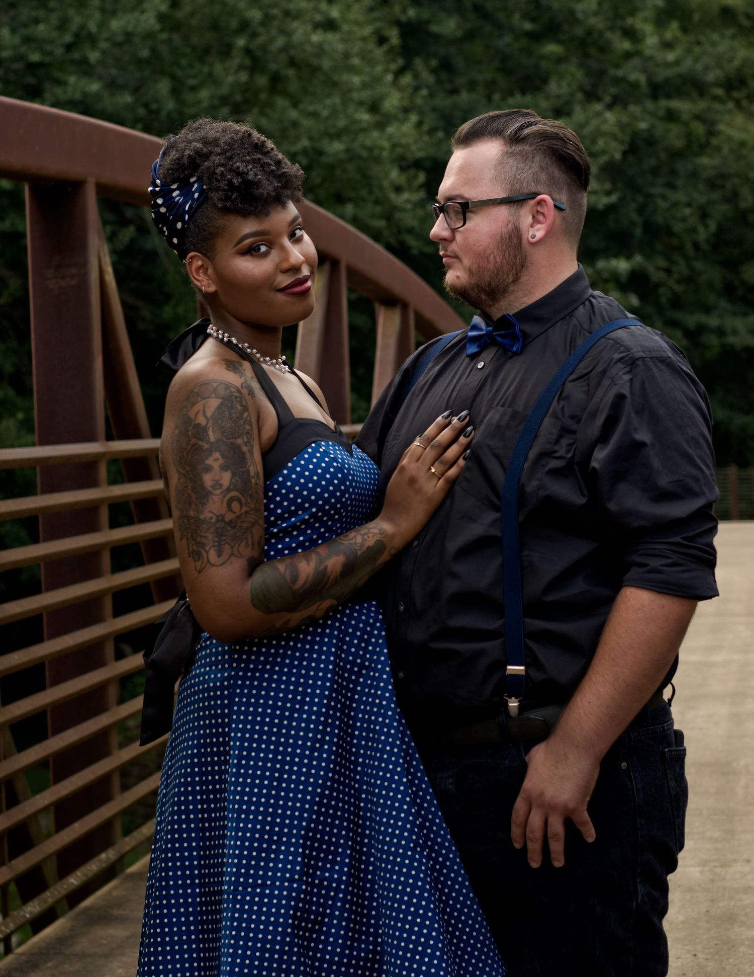 Engagement portrait of interracial couple in 1950s-inspired attire at Hayes Nature Preserve bridge, standing close together and smiling.