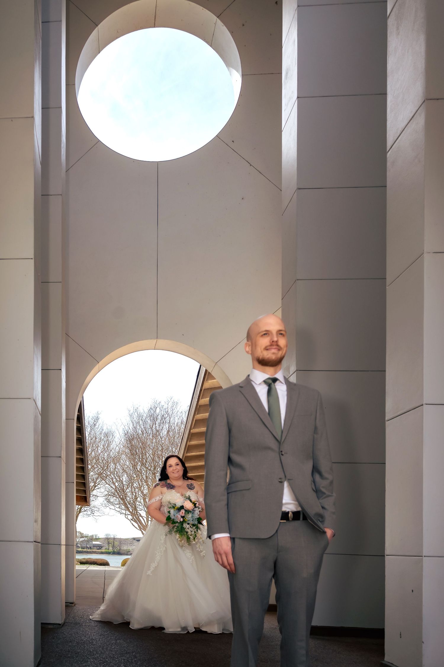 Editorial shot of bride walking up behind groom with unique architectural background, photographed by Catch Your Fire Photography.