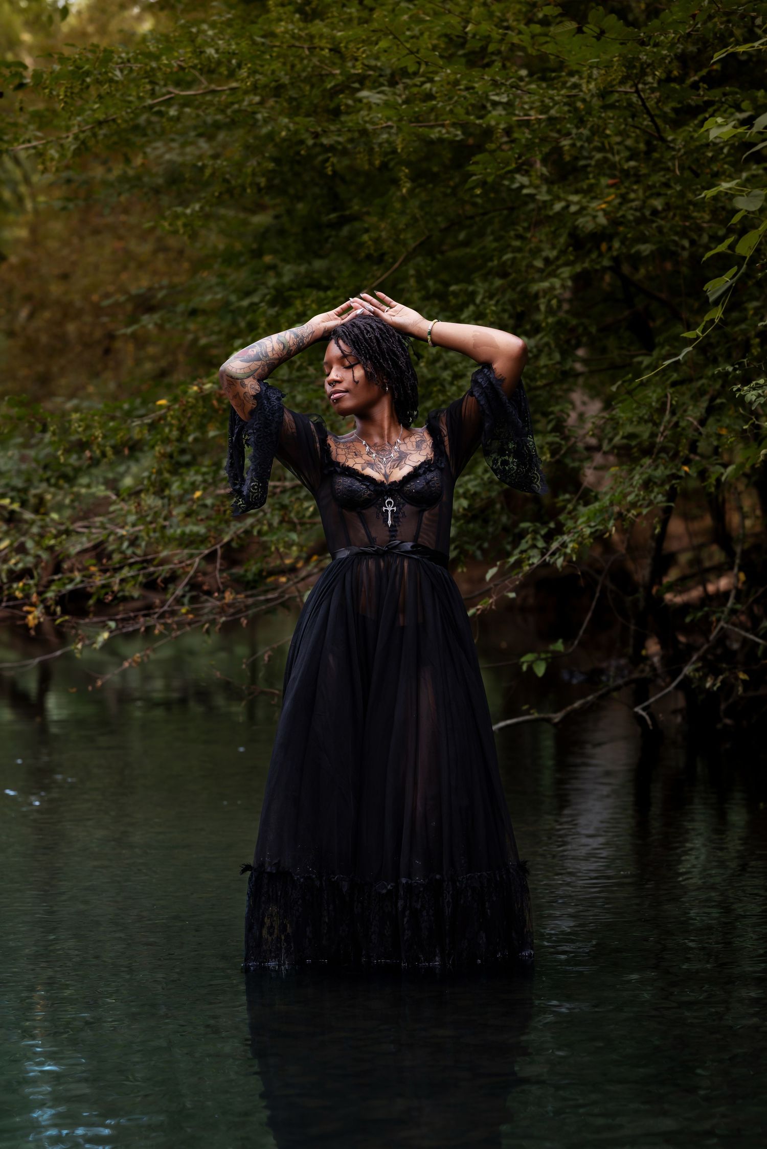 Candid moment of a young woman standing in a creek, arms above her head, eyes closed, enjoying the sounds of nature in Huntsville, Alabama.