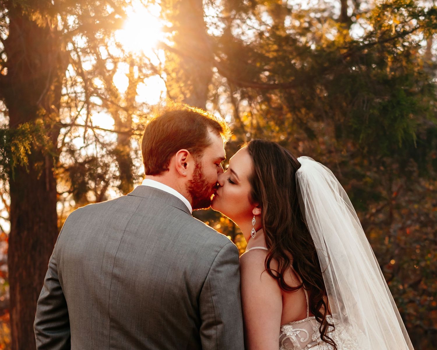 Golden hour wedding portrait with sun flare glowing through trees as couple kisses at Monte Sano Lodge