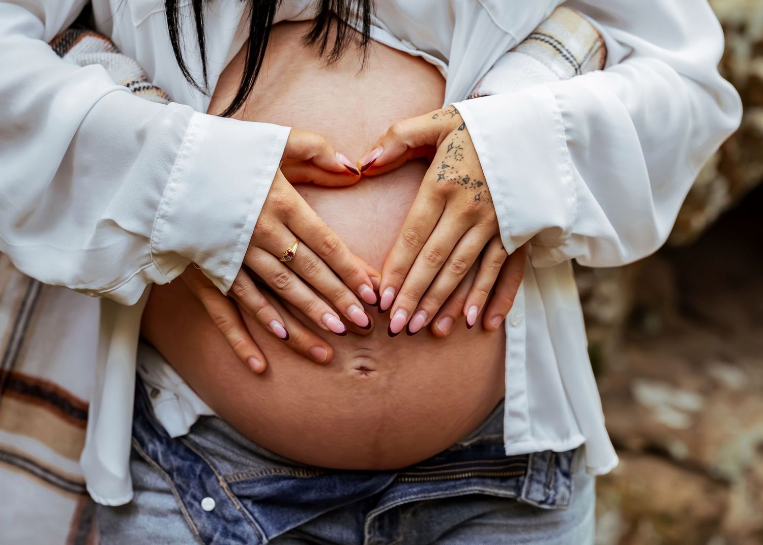 closeup shot of bare pregnant belly with mom  and dads hands on belly making a heart shape captured by Catch Your Fire Photography