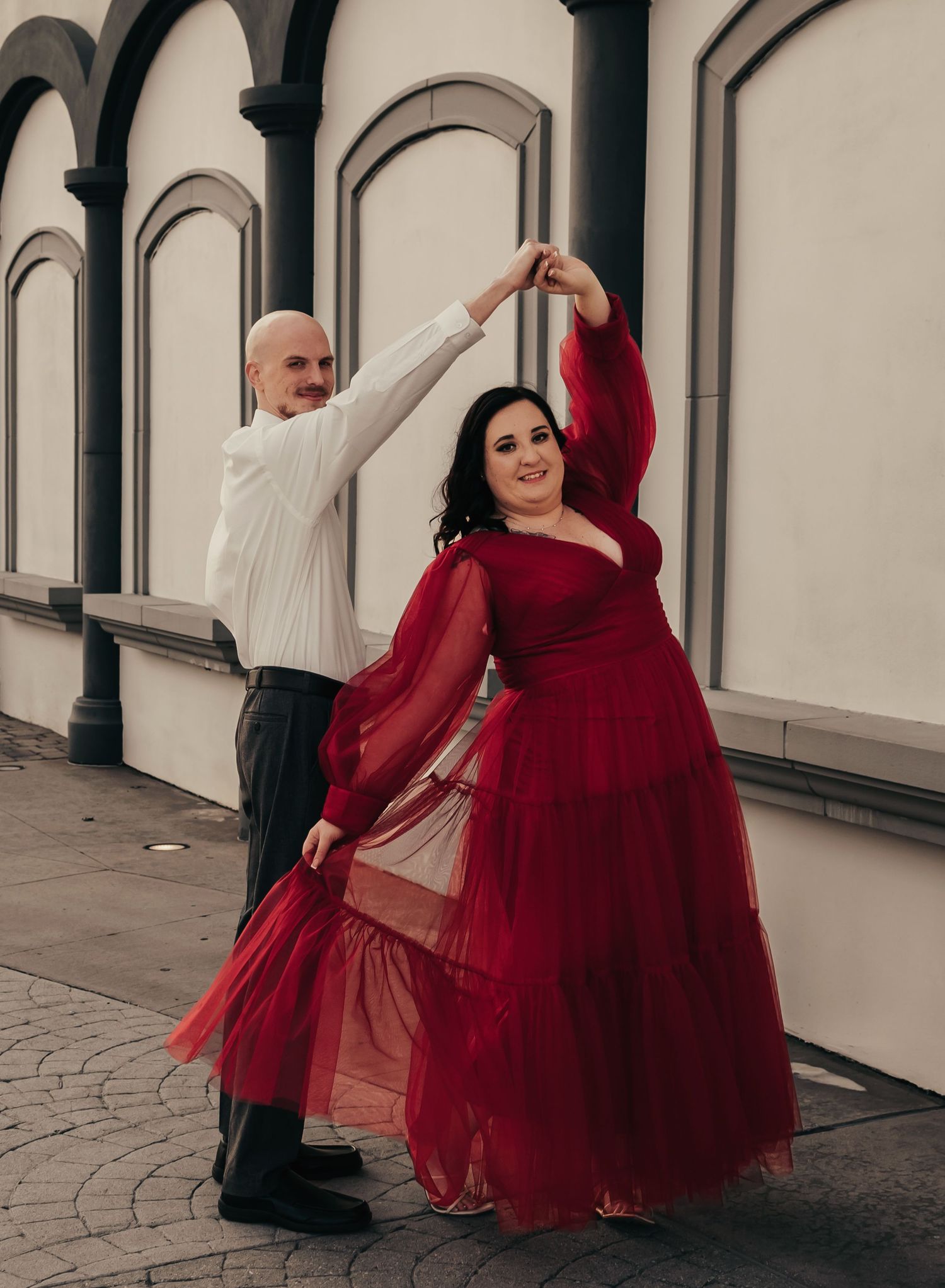 Engagement couple dancing on Bridge Street sidewalk, bride in red gown, captured by Catch Your Fire Photography.