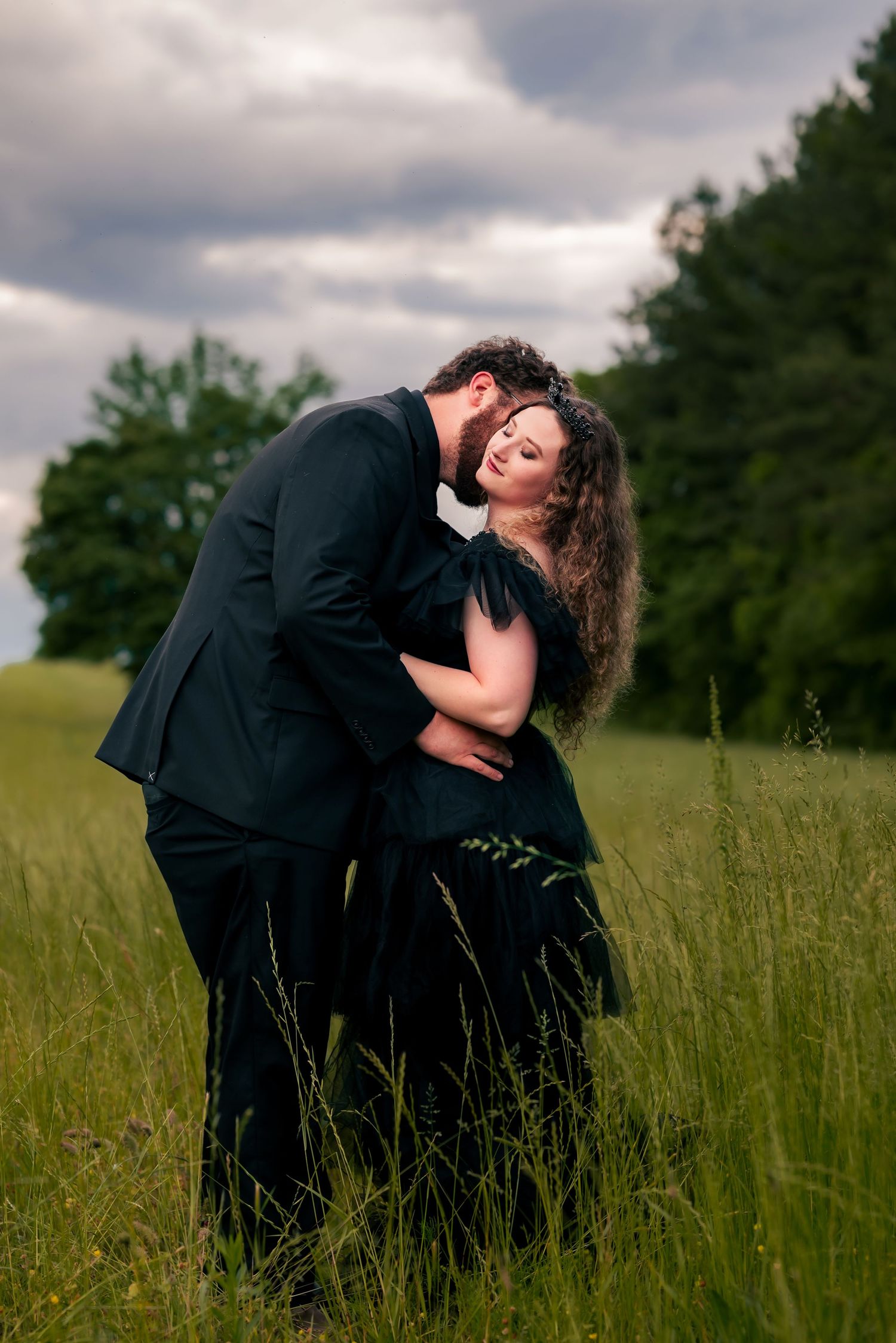 Editorial-style wedding photo of couple in black dress, intimate neck kiss in overgrown field, photographed by Catch Your Fire Photography.