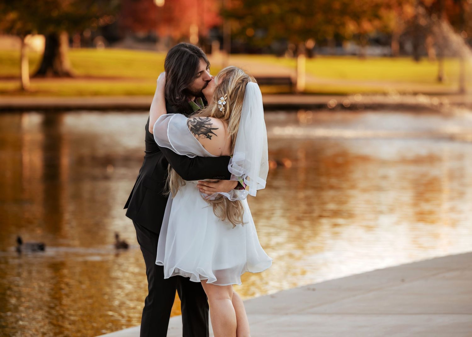 Downtown elopement at Huntsville Big Spring Park during golden hour with couple kissing beside pond and ducks swimming nearby in fall