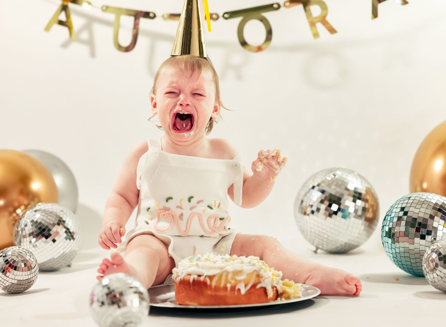 studio cake smash for one year old girl who is screaming, sitting in front of disco balls, captured by Catch Your Fire Photography in AL.
